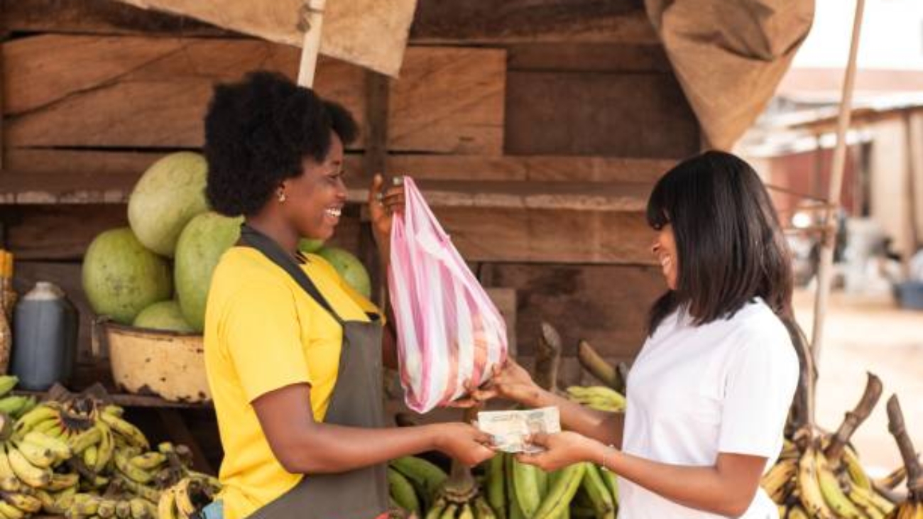 Two African women in a market paying with cash